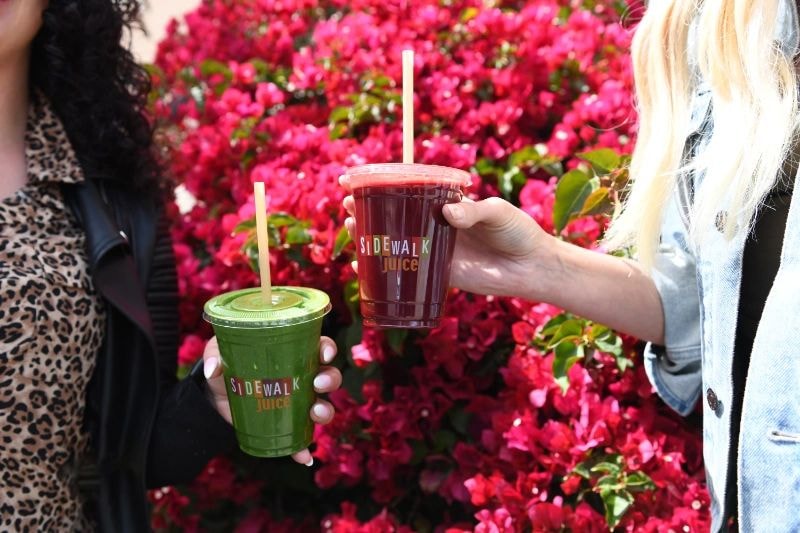 Sidewalk Juices branded cups in front of pink flower wall